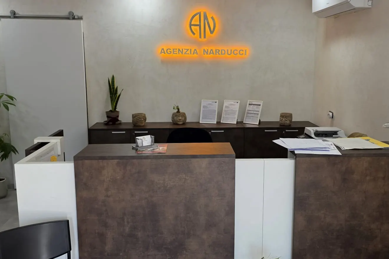 Il bancone della reception dell'Agenzia Narducci, col logo illuminato sulla parete